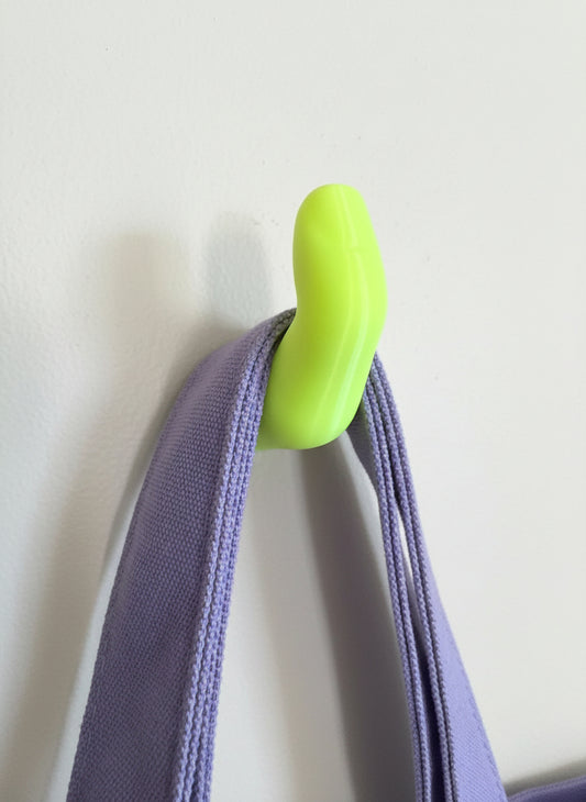 Neon Yellow finger hook screwed into a white wall holding a Purple bag handle 